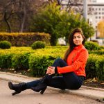 Young nice girl in vibrant orange jacket walking in autumn city