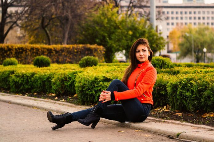 Young nice girl in vibrant orange jacket walking in autumn city