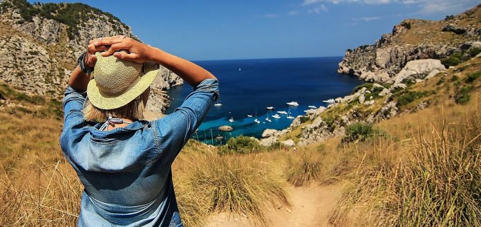 girl wearing denim jacket straw hat looking down at harbor from hill