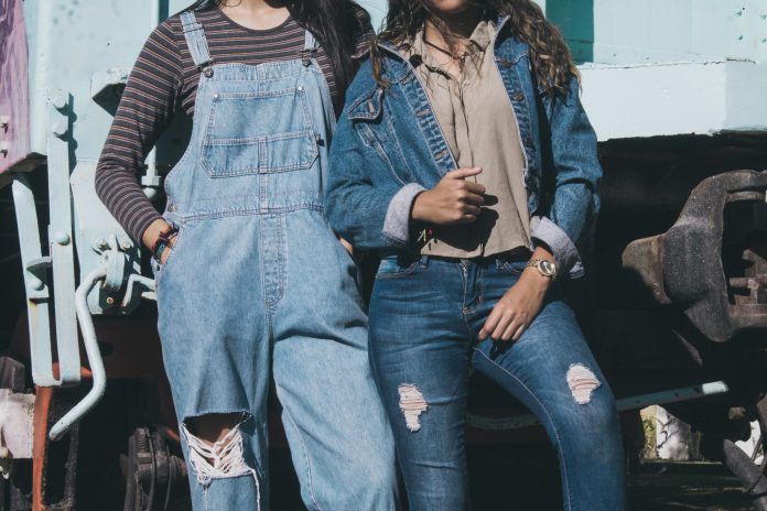 two women standing side by side wearing denim dungarees and denim jacket