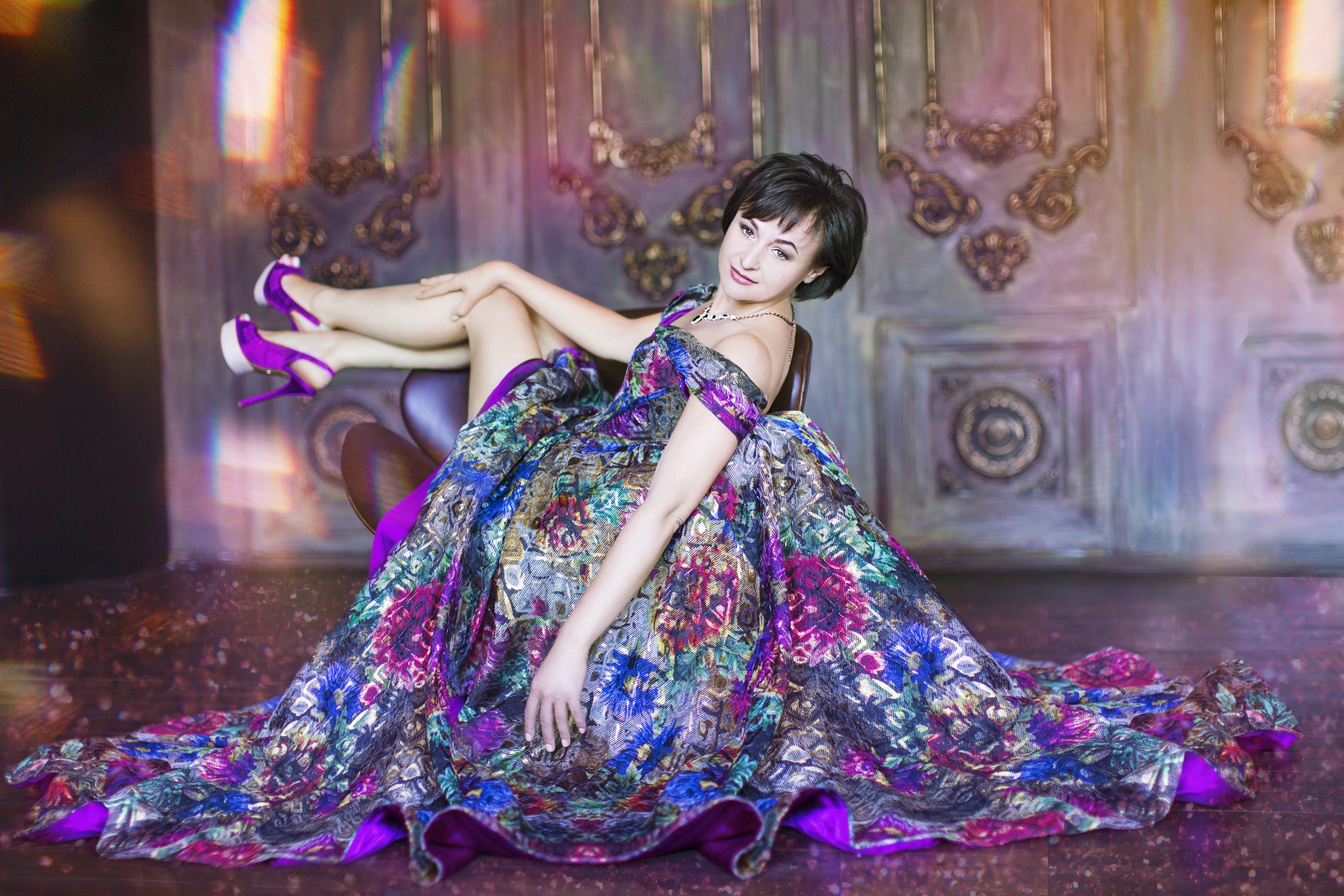 purple fashion design outfits - stock photo model posing on chair wearing ornate purple floral dress