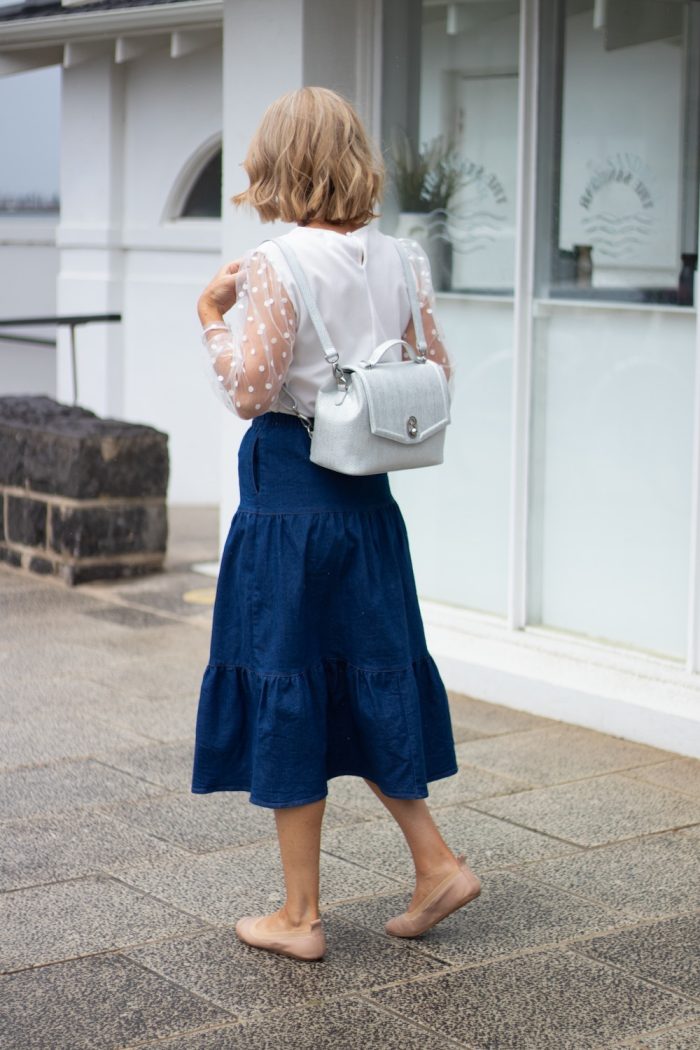 woman walking down a sidewalk carrying a white purse on her back